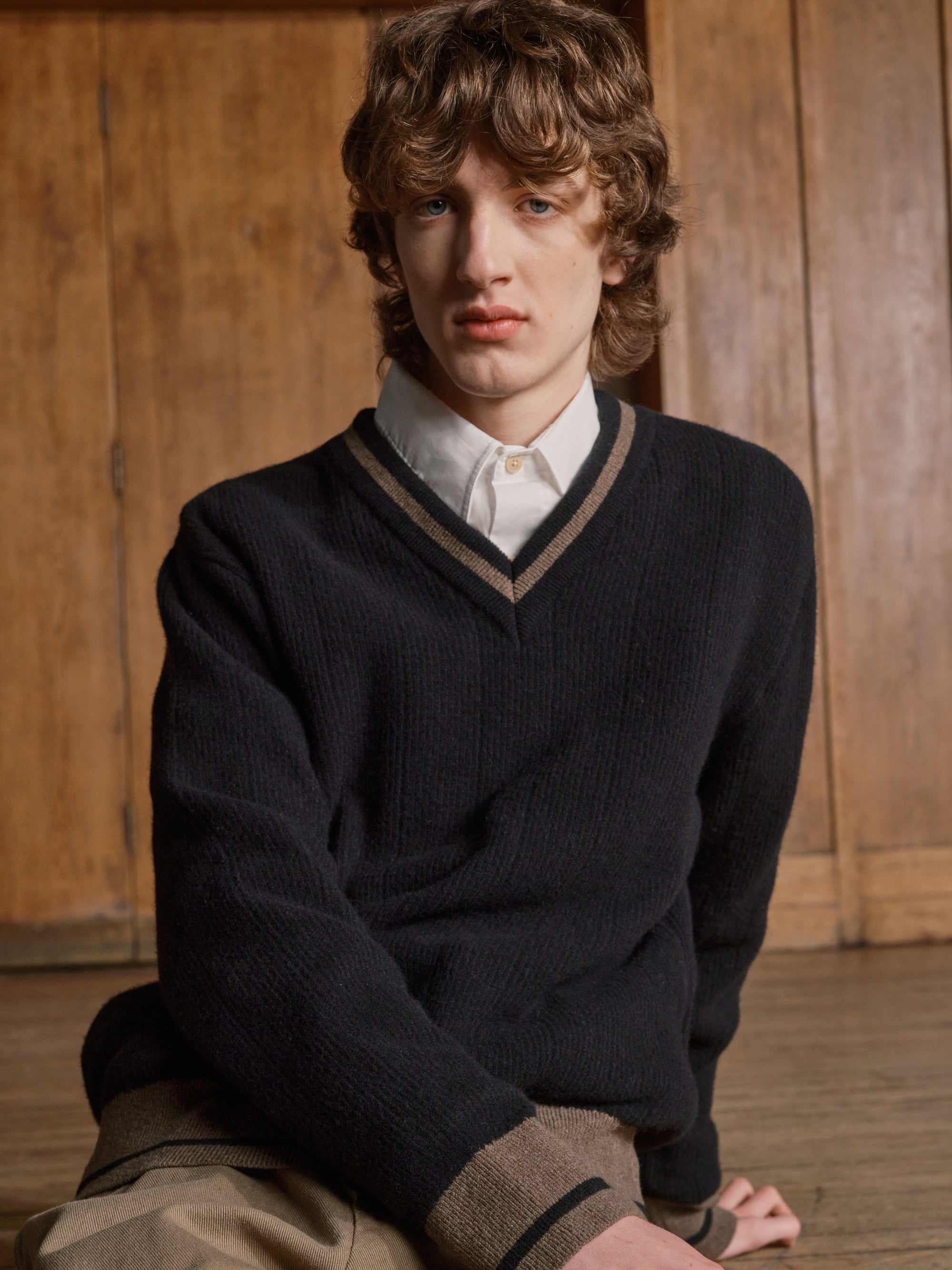 Model in a black V neck jumper and white shirt, seated